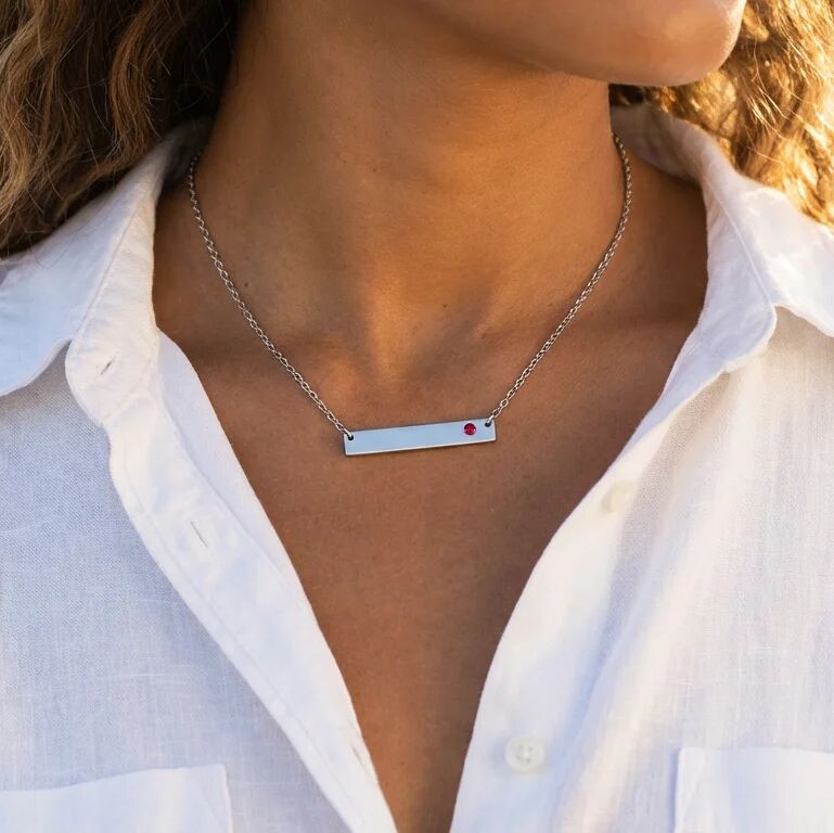 Necklace with a small red gemstone worn by a person in a white shirt.